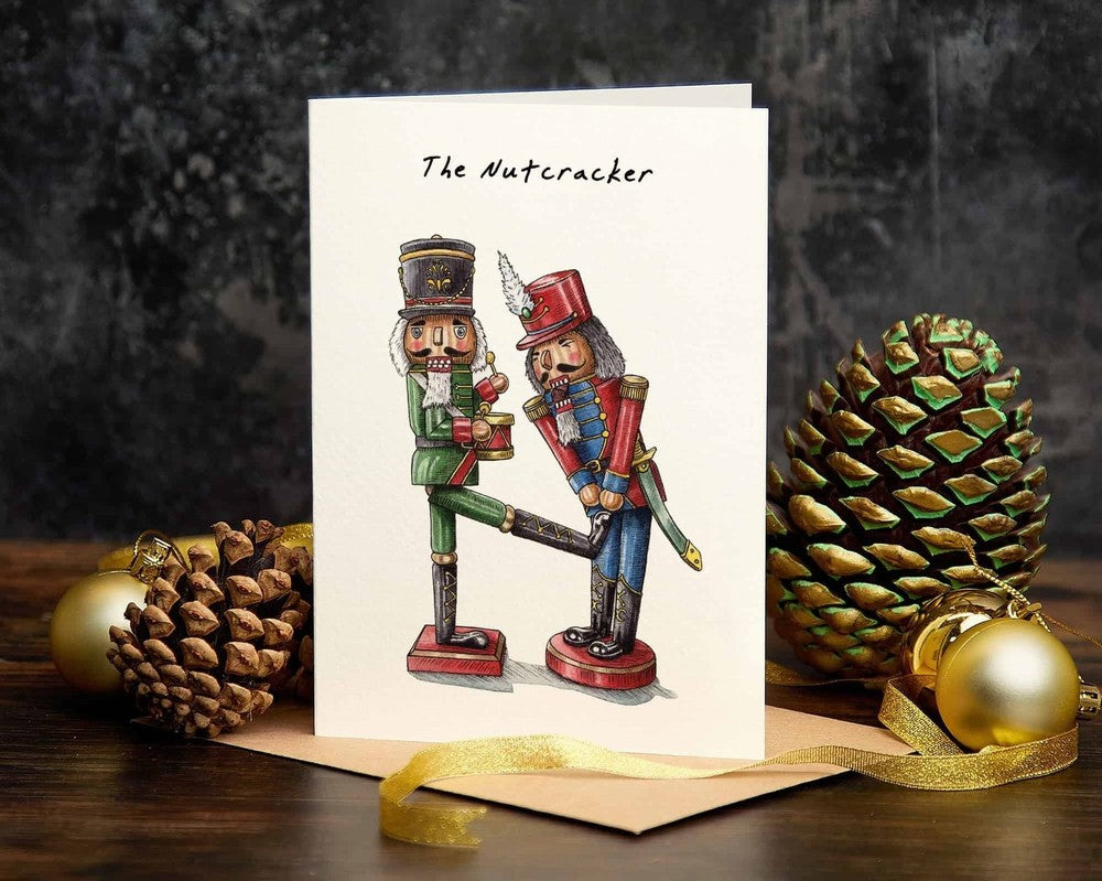 Greeting card with 'The Nutcracker' design featuring two nutcrackers, surrounded by pine cones and ornaments on a dark background.