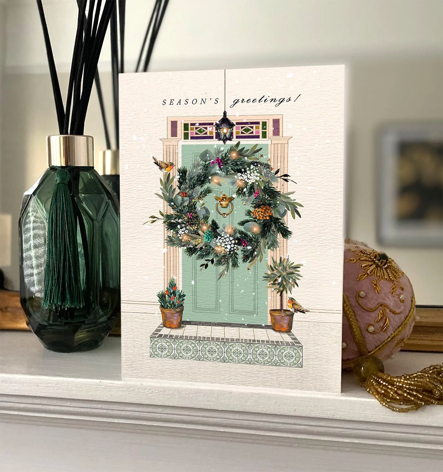 Christmas card with decorative wreath on a door, placed on a surface with decorative items.